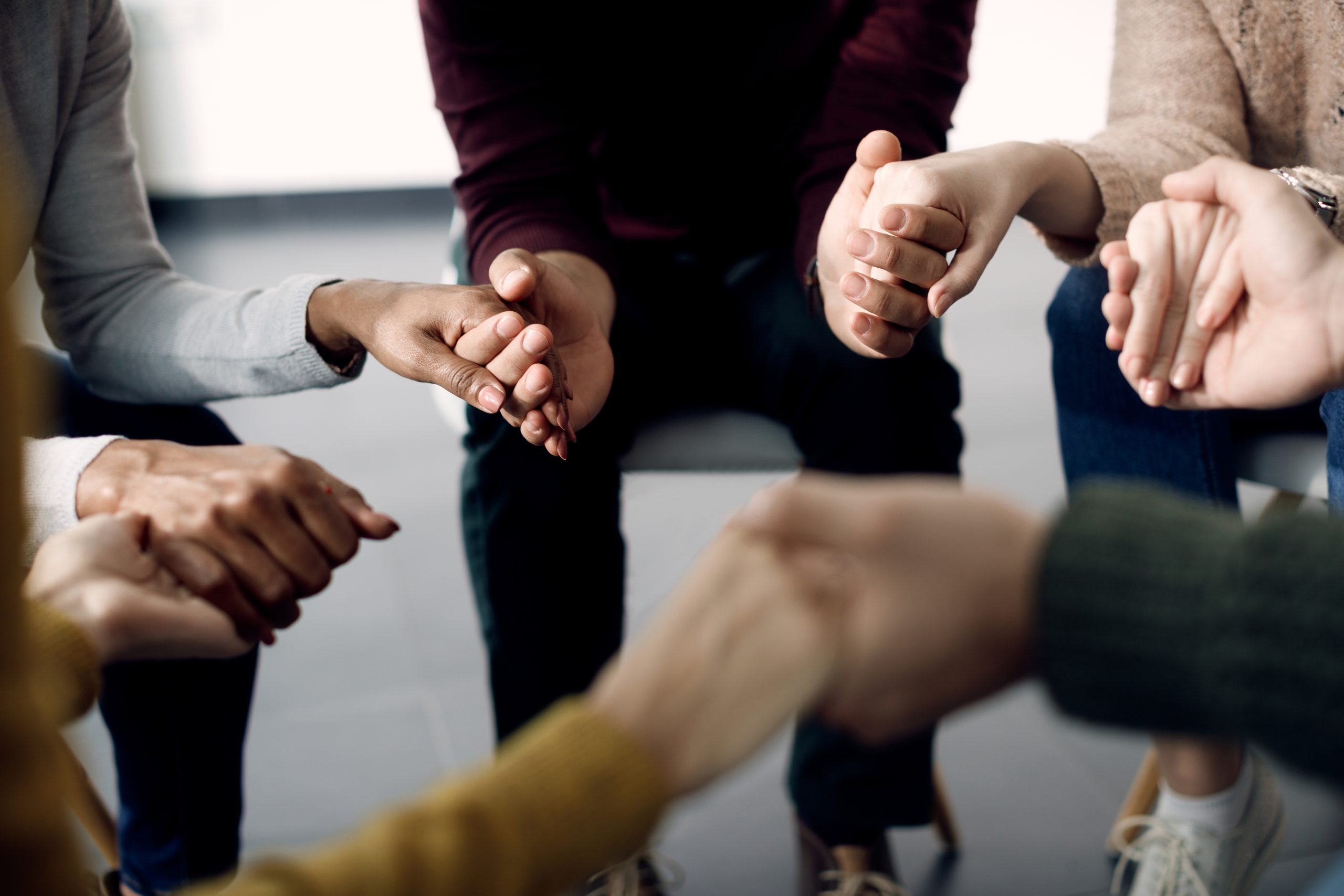 Close-up of people holding hands while attending group therapy.